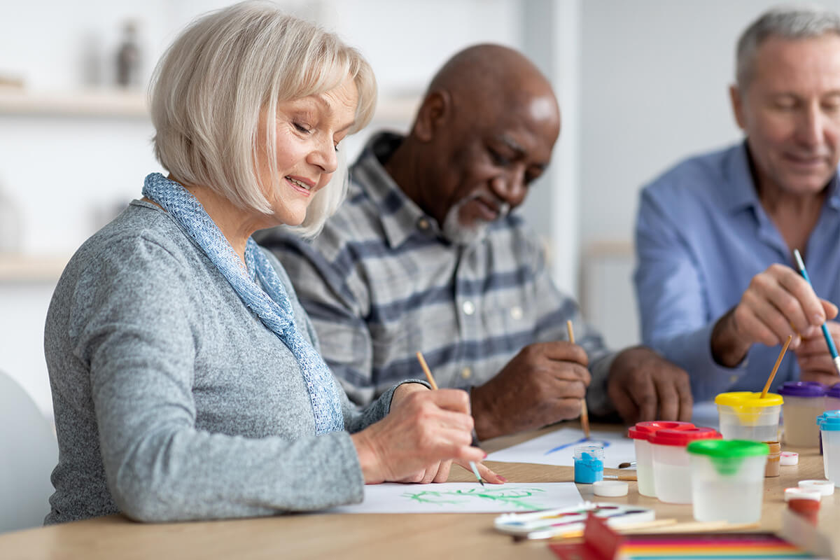 Woman smiling as she and two men paint pictures at a table