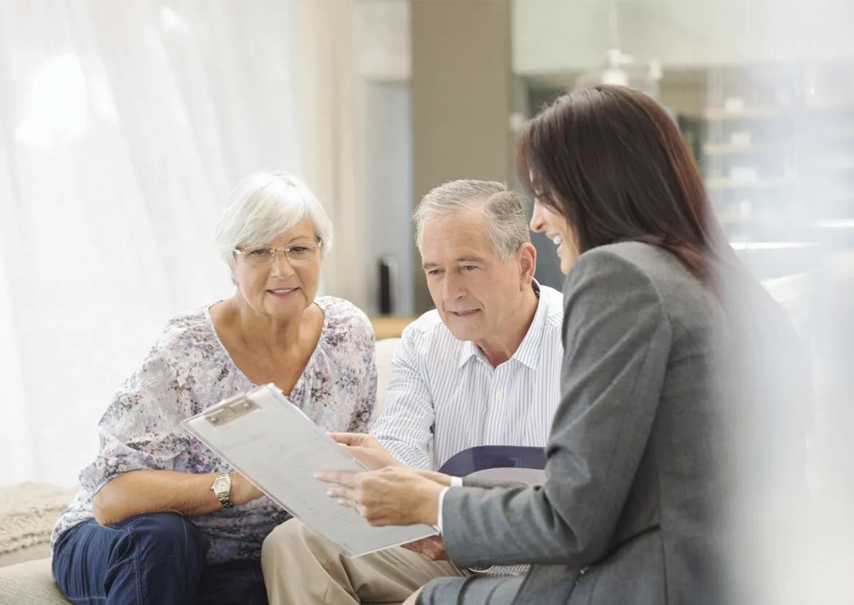 Senior couple speaking to professional who is showing them papers on a clipboard